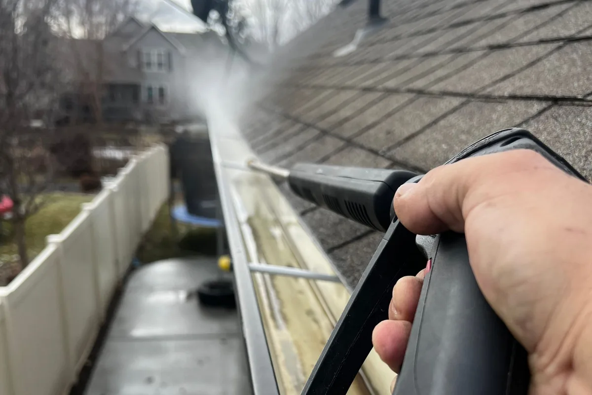 Flushing debris from the gutter along a shingle roof edge in Port Jefferson