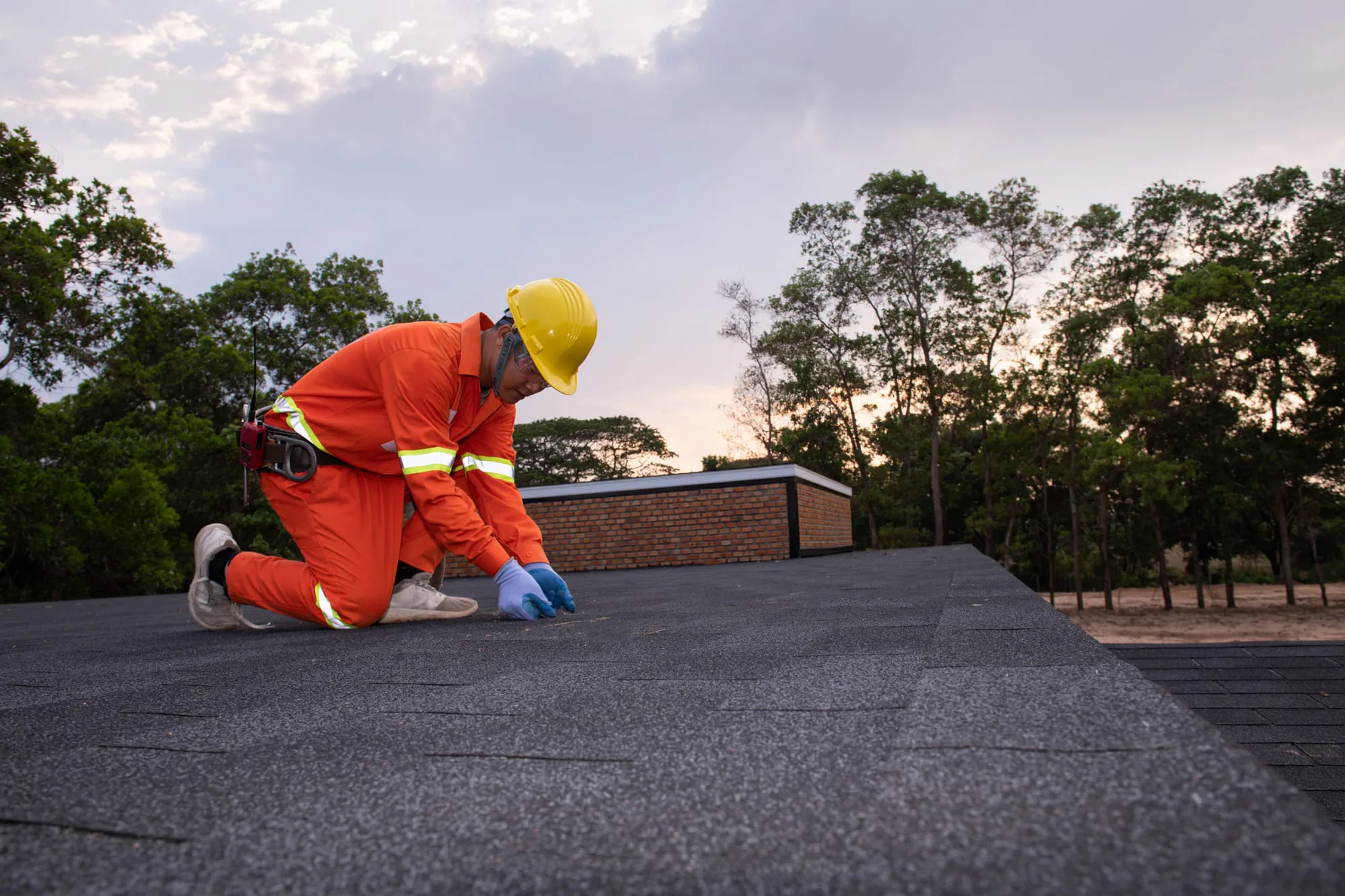Roofer inspecting an asphalt shingle roof at sunset