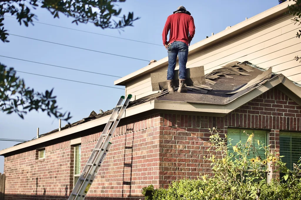 Roofing contractor on a residential roof with a ladder set against the eave